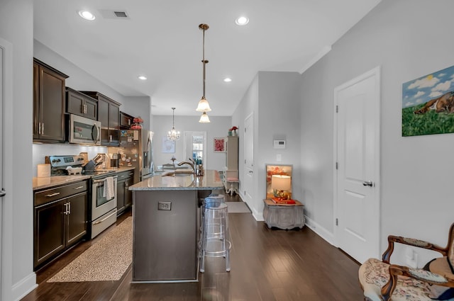 kitchen with a breakfast bar area, hanging light fixtures, stainless steel appliances, light stone countertops, and an island with sink