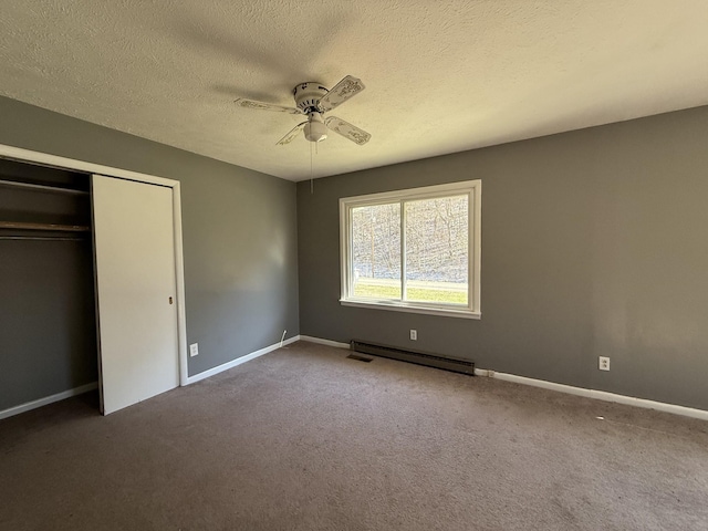 unfurnished bedroom featuring a baseboard radiator, a textured ceiling, a closet, and dark colored carpet