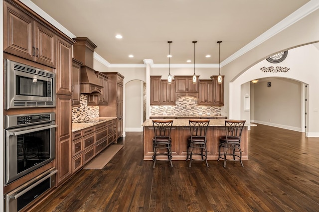 kitchen with pendant lighting, a center island, light stone counters, stainless steel appliances, and custom range hood