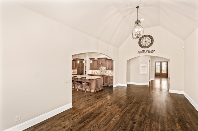 unfurnished living room featuring dark wood-type flooring, a chandelier, high vaulted ceiling, and french doors