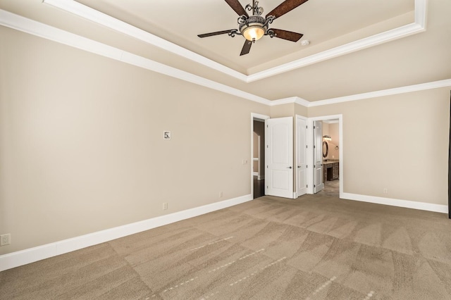 unfurnished bedroom featuring ensuite bath, ornamental molding, a tray ceiling, and carpet