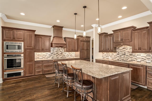 kitchen featuring appliances with stainless steel finishes, sink, hanging light fixtures, a center island, and custom range hood