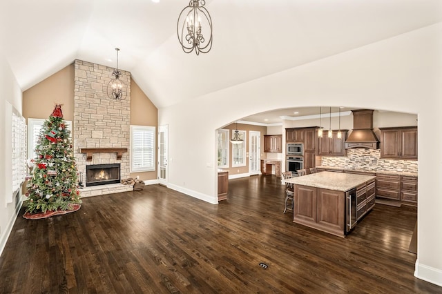 kitchen with premium range hood, a stone fireplace, a center island, hanging light fixtures, and stainless steel microwave