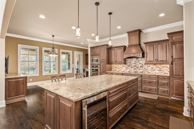 kitchen with appliances with stainless steel finishes, wine cooler, light stone countertops, custom range hood, and a kitchen island