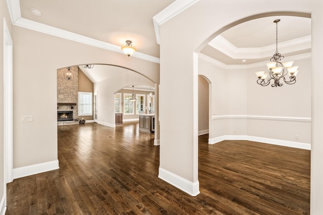 empty room featuring a stone fireplace, dark hardwood / wood-style floors, a raised ceiling, crown molding, and an inviting chandelier