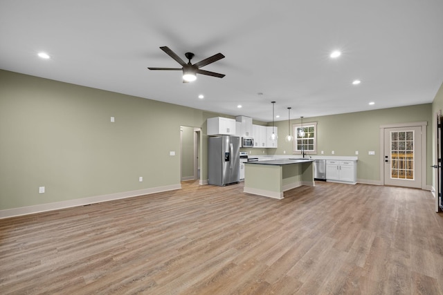 kitchen featuring appliances with stainless steel finishes, white cabinetry, hanging light fixtures, a center island, and light wood-type flooring