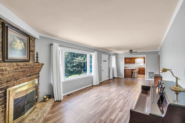 living room featuring ornamental molding, a brick fireplace, a wealth of natural light, and light wood-type flooring