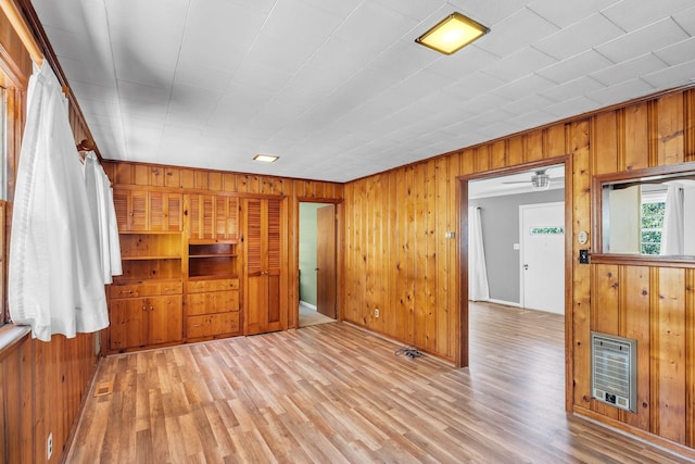 unfurnished living room featuring heating unit, light hardwood / wood-style flooring, and wood walls