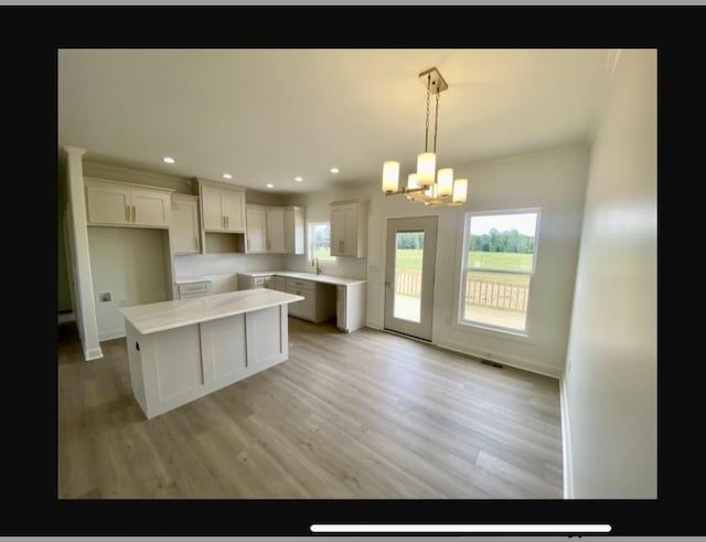 kitchen with an inviting chandelier, hanging light fixtures, a center island, light hardwood / wood-style floors, and white cabinets