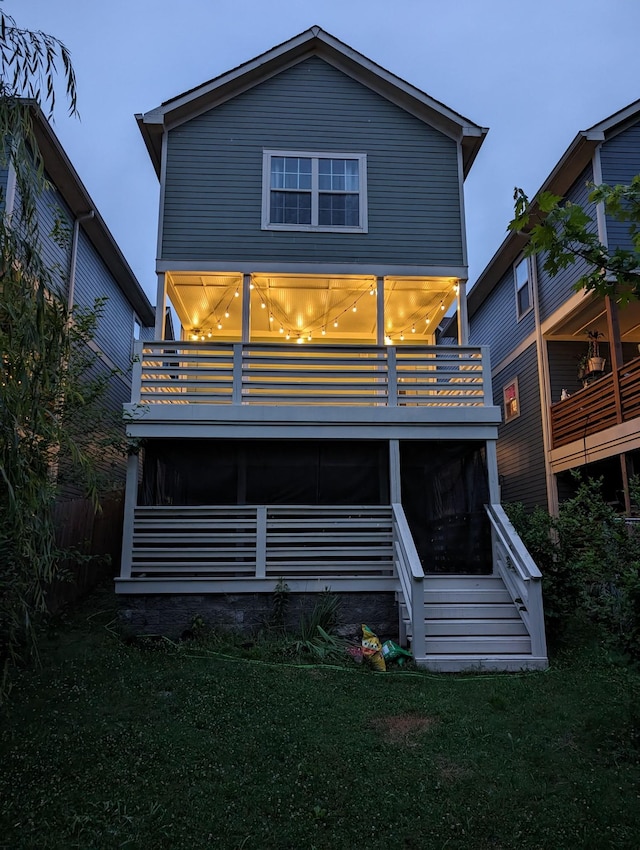 back house at dusk featuring a balcony, a sunroom, and a yard