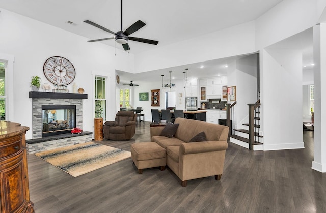 living room featuring ceiling fan, a fireplace, dark hardwood / wood-style floors, and a high ceiling