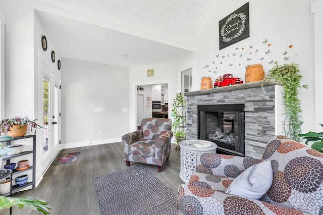 living room featuring vaulted ceiling, a stone fireplace, and wood-type flooring