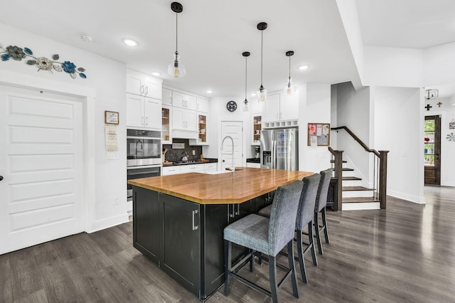 kitchen with pendant lighting, butcher block countertops, white cabinets, a kitchen island with sink, and stainless steel fridge with ice dispenser