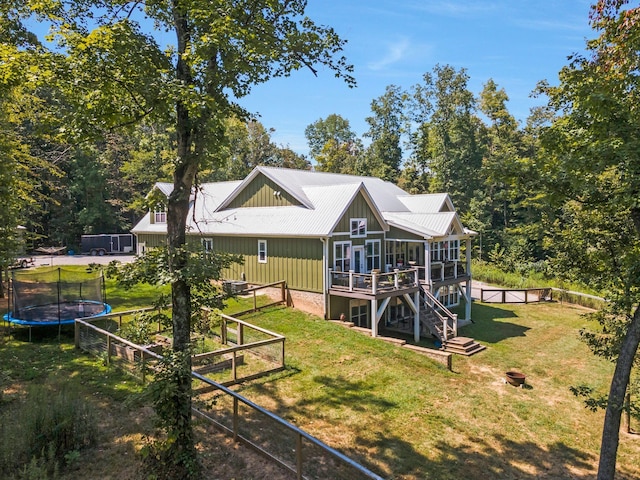 back of house featuring a trampoline, a wooden deck, a lawn, and a sunroom