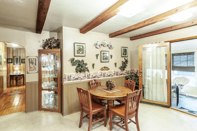 dining space with beam ceiling, a textured ceiling, and wood walls