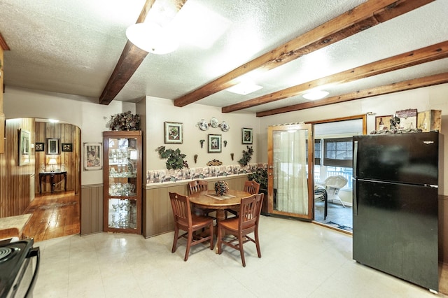 dining area with beamed ceiling, a textured ceiling, and wood walls