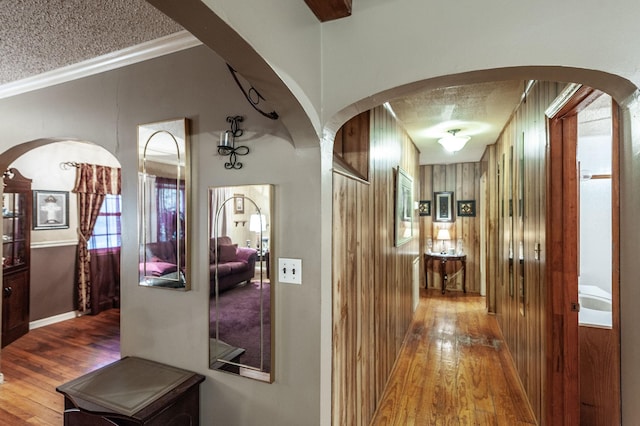 hallway featuring crown molding, wood-type flooring, a textured ceiling, and wood walls