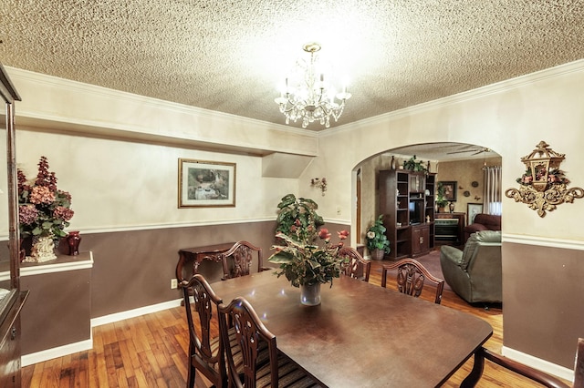 dining room featuring a notable chandelier, crown molding, wood-type flooring, and a textured ceiling