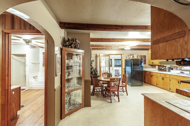 kitchen featuring sink, a textured ceiling, black refrigerator, beamed ceiling, and ceiling fan