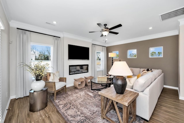 living room with visible vents, dark wood-type flooring, crown molding, and a glass covered fireplace