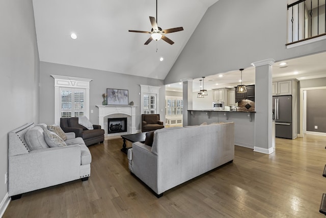 living room featuring ornate columns, high vaulted ceiling, hardwood / wood-style flooring, ceiling fan, and a premium fireplace