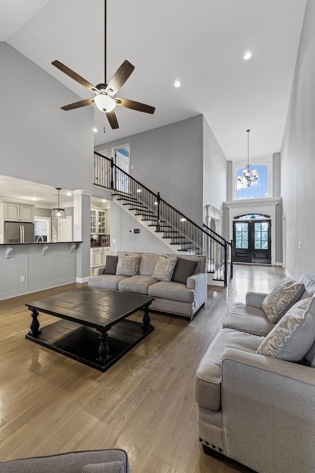 living room with ceiling fan with notable chandelier, wood-type flooring, and a high ceiling