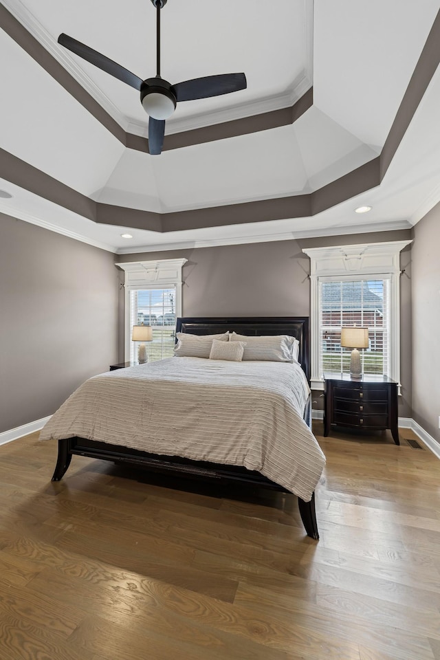 bedroom featuring a raised ceiling, crown molding, ceiling fan, and light wood-type flooring