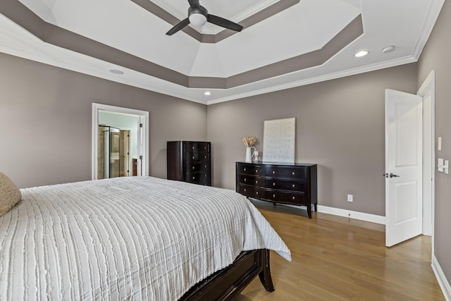 bedroom with crown molding, light hardwood / wood-style flooring, ensuite bath, ceiling fan, and a raised ceiling