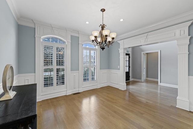 unfurnished dining area featuring ornamental molding, light hardwood / wood-style floors, decorative columns, and a notable chandelier