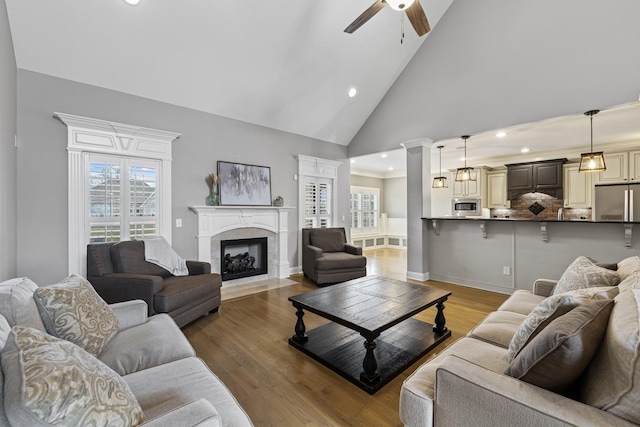 living room featuring a tile fireplace, ceiling fan, hardwood / wood-style floors, decorative columns, and high vaulted ceiling