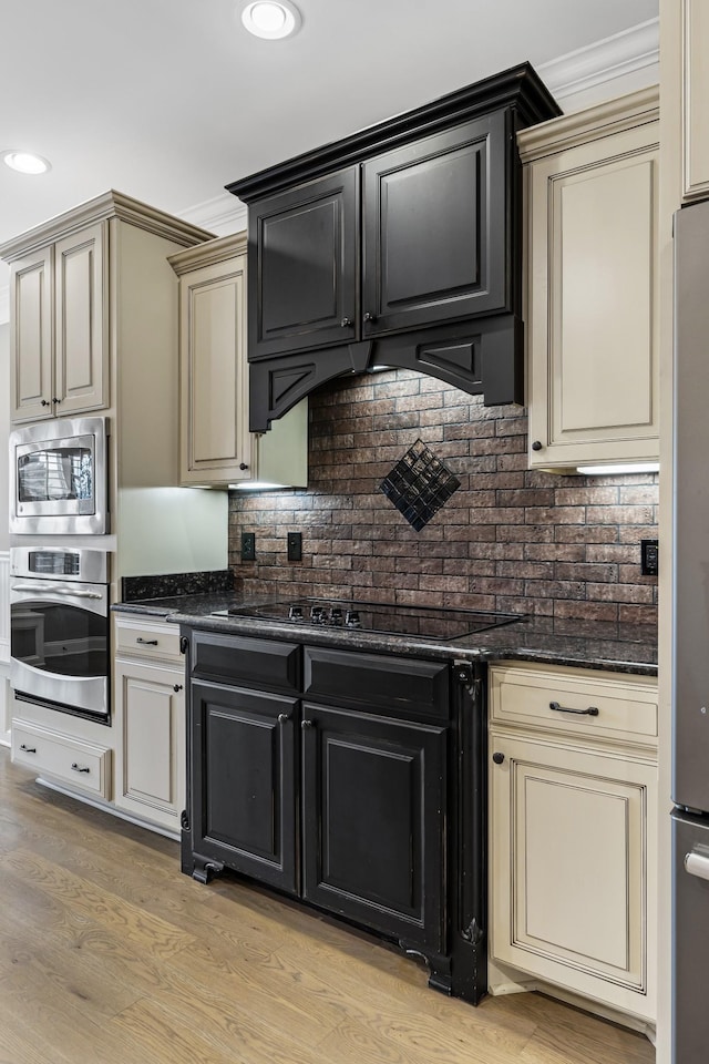 kitchen featuring stainless steel appliances, cream cabinets, dark stone countertops, and light hardwood / wood-style flooring