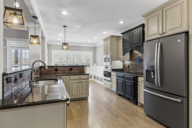 kitchen with appliances with stainless steel finishes, sink, pendant lighting, and cream cabinetry