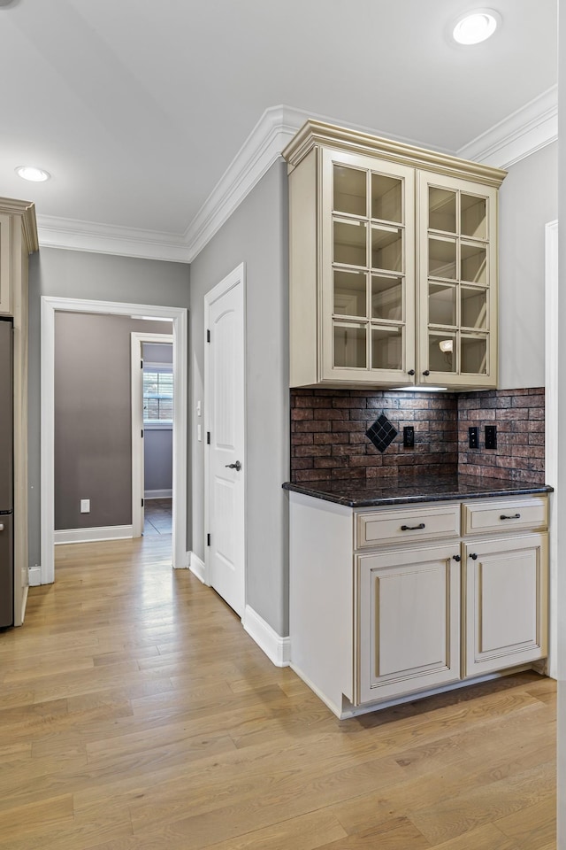 bar with dark stone countertops, cream cabinets, stainless steel fridge, and ornamental molding