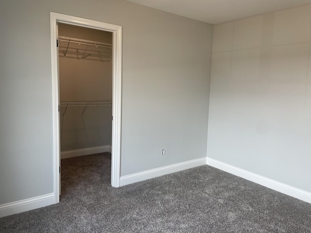 unfurnished bedroom featuring dark carpet, a walk in closet, and a closet