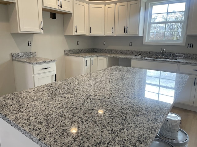 kitchen featuring light stone countertops, sink, and white cabinets