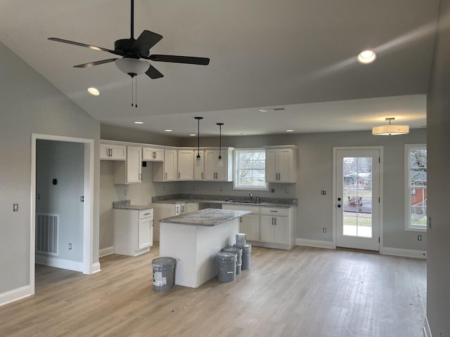 kitchen with sink, a center island, hanging light fixtures, light stone countertops, and white cabinets