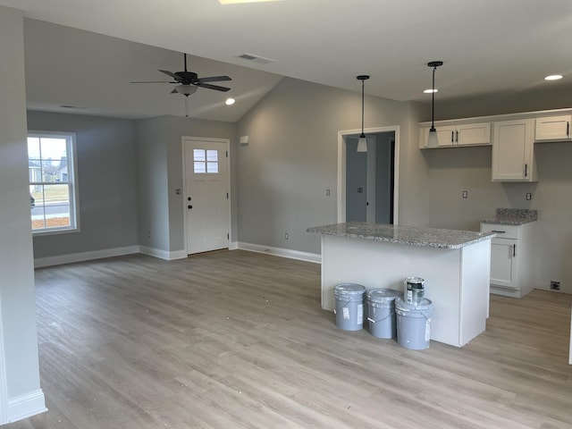 kitchen with a kitchen island, light stone countertops, white cabinets, and decorative light fixtures