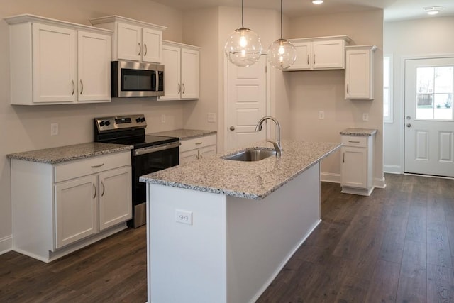 kitchen featuring sink, white cabinets, stainless steel appliances, light stone countertops, and a center island with sink