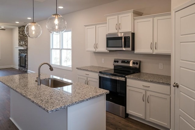 kitchen featuring pendant lighting, sink, white cabinetry, stainless steel appliances, and an island with sink