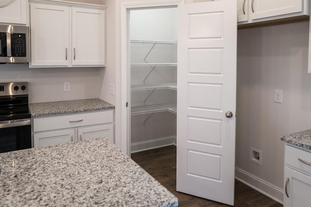 kitchen featuring stainless steel appliances, white cabinetry, light stone countertops, and dark hardwood / wood-style floors