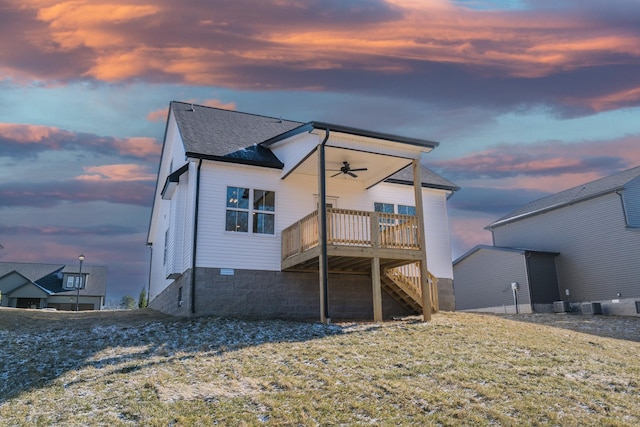 back house at dusk with a wooden deck, ceiling fan, and a lawn