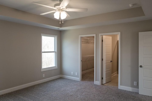 unfurnished bedroom with a tray ceiling, a walk in closet, light colored carpet, and a closet