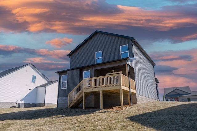 back house at dusk featuring a wooden deck and a lawn