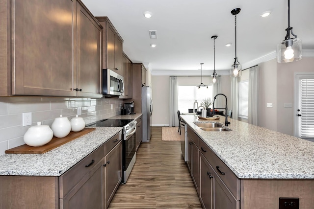 kitchen with an island with sink, light stone counters, decorative light fixtures, stainless steel appliances, and a sink