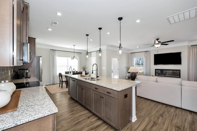 kitchen with visible vents, light stone counters, hanging light fixtures, a kitchen island with sink, and a sink