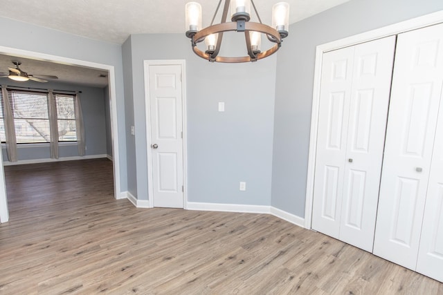 unfurnished dining area with ceiling fan with notable chandelier, a textured ceiling, and light hardwood / wood-style flooring