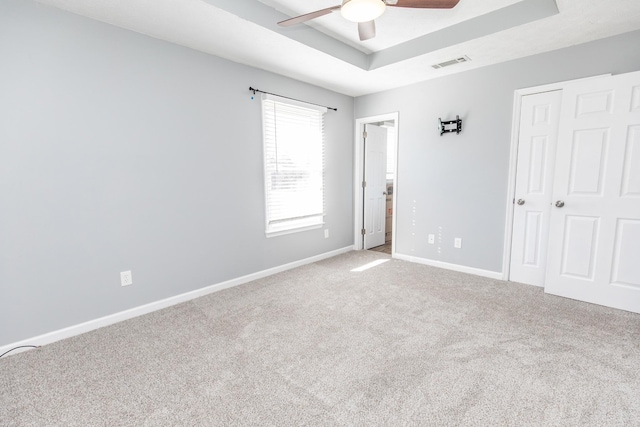 carpeted empty room featuring a raised ceiling and ceiling fan