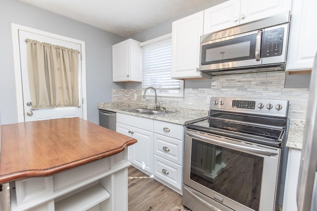 kitchen featuring sink, white cabinets, decorative backsplash, stainless steel appliances, and light stone countertops