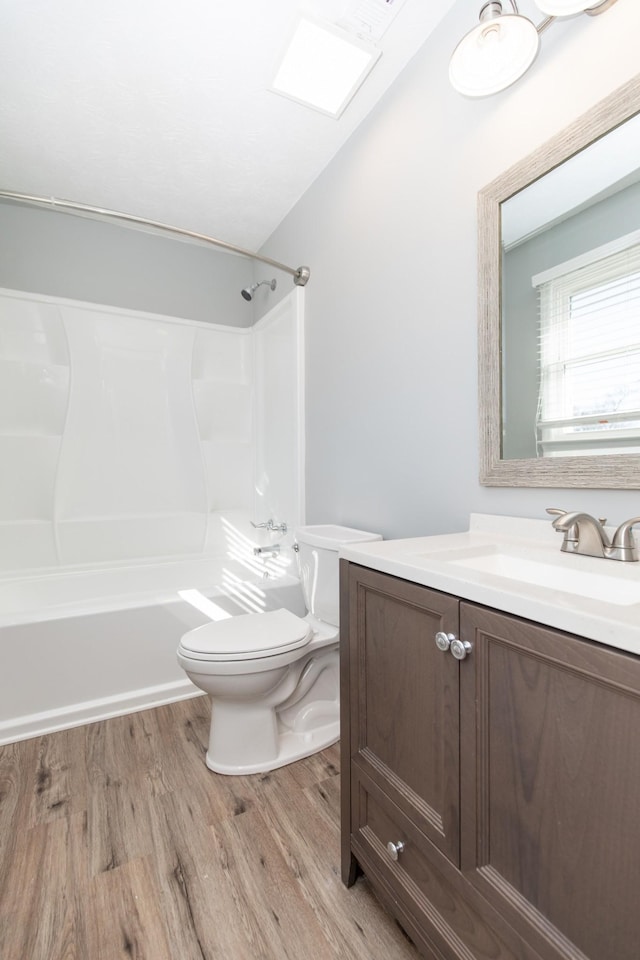 full bathroom with tub / shower combination, hardwood / wood-style floors, lofted ceiling with skylight, vanity, and toilet