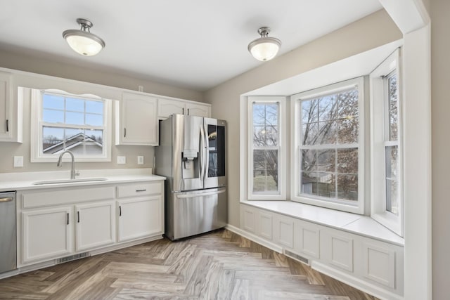 kitchen featuring sink, appliances with stainless steel finishes, white cabinetry, a wealth of natural light, and light parquet flooring